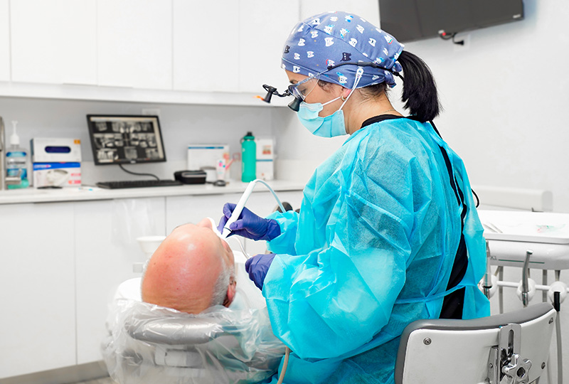 A dental hygienist in full protective gear is cleaning a patient s teeth in a professional setting.