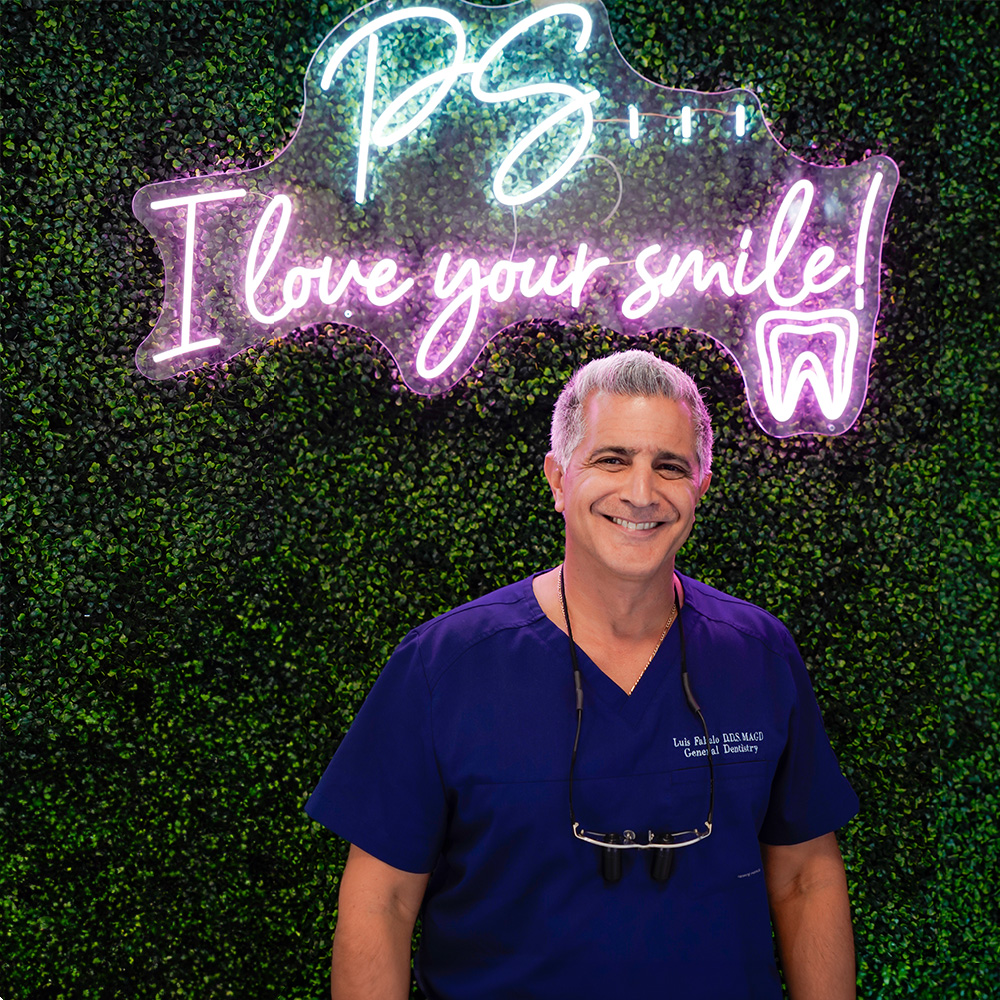 A smiling man wearing a white lab coat stands in front of a sign with the letters GF on it.