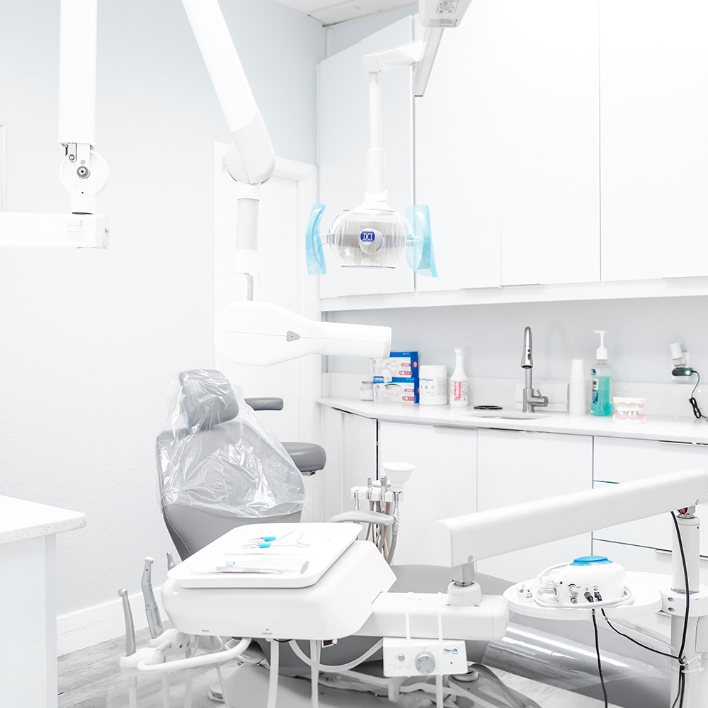 An interior view of a dental office with a large dental chair, dental equipment, and various tools on a countertop next to an open door.